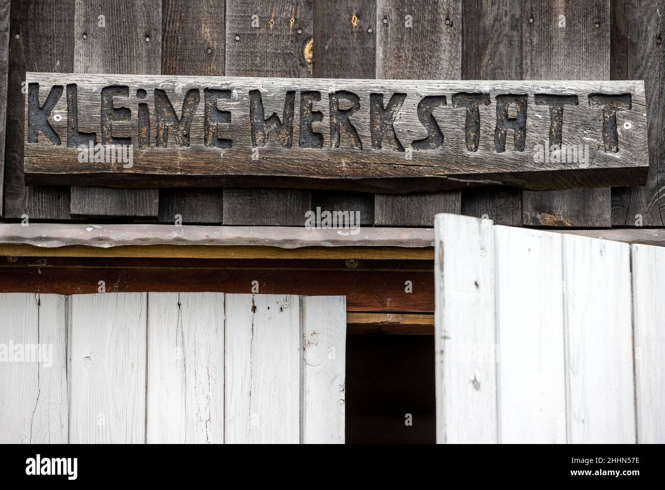 25 gennaio 2022, Meclemburgo-Pomerania occidentale, Greifswald: Sopra il cancello d'ingresso del cantiere del museo è appesa una targa di legno con l'iscrizione "officina piccola". La Camera dell'artigianato del Meclemburgo-Pomerania occidentale (HWK) ha premiato la società di formazione Greifswald con il vincitore nazionale del Concorso artigianale tedesco nel settore della costruzione di imbarcazioni. Secondo la HWK, 58 società che operano nel settore navale e navale sono registrate nella sua giurisdizione. Foto: Jens Büttner/dpa-Zentralbild/dpa Foto Stock