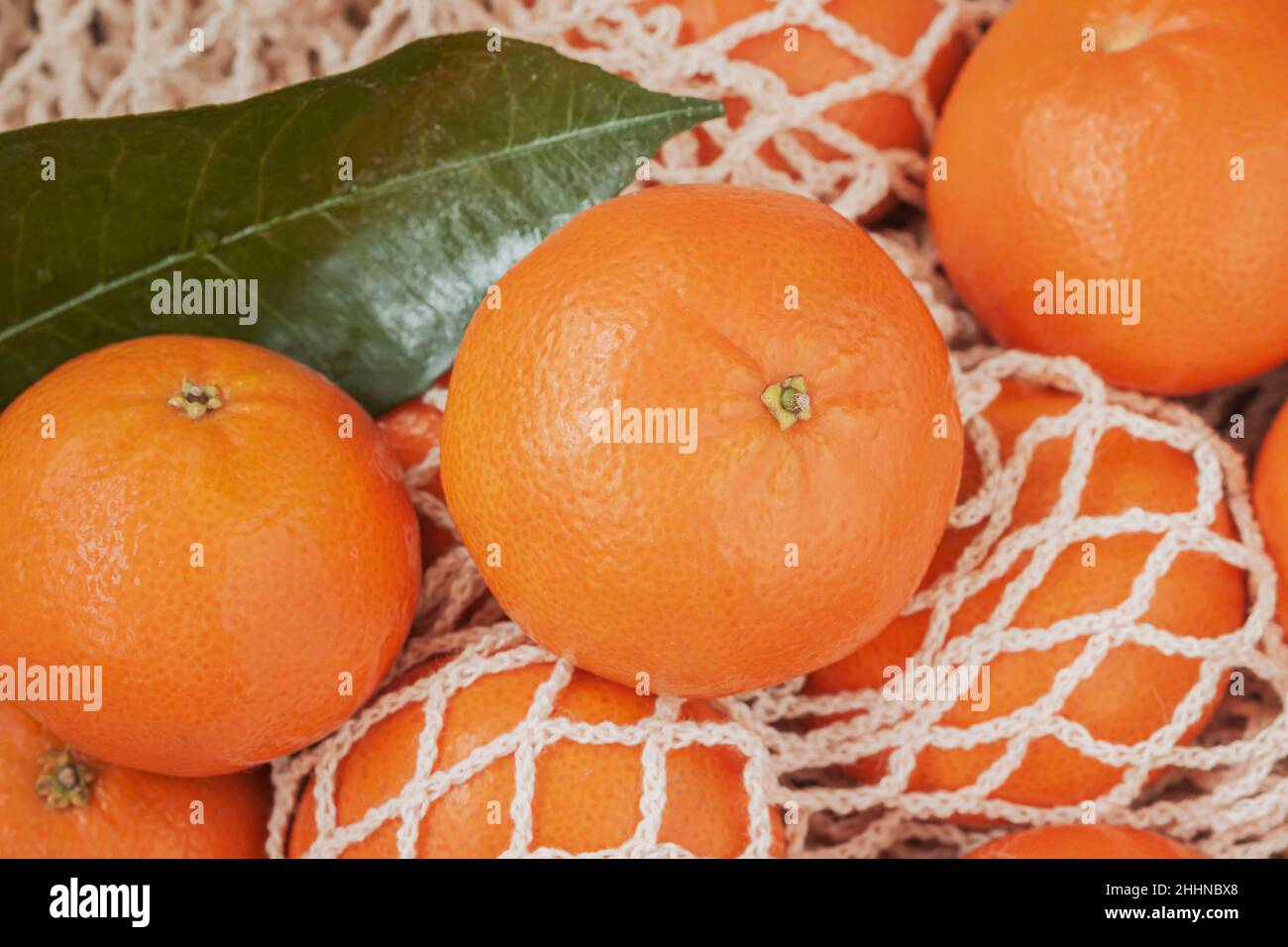 Frutta d'arancia di agrumi con foglie verdi su sacchetto di cotone a rete. Mandarino, arance tangerine. Stile di vita sano, concetto di disintossicazione Foto Stock