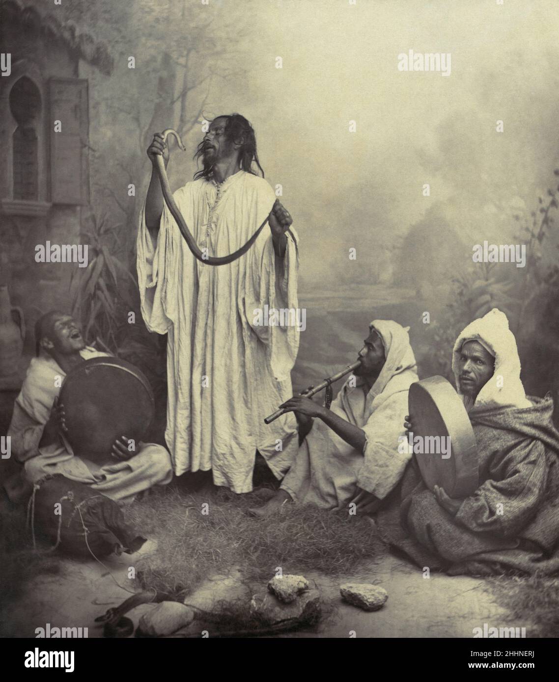 Incantatore di serpenti - Tancrède Dumas - l'uomo marocchino tiene un serpente in piedi con un gruppo di musicisti seduti. Un giocatore di flauto e due batteristi a mano-1860-1890 Foto Stock
