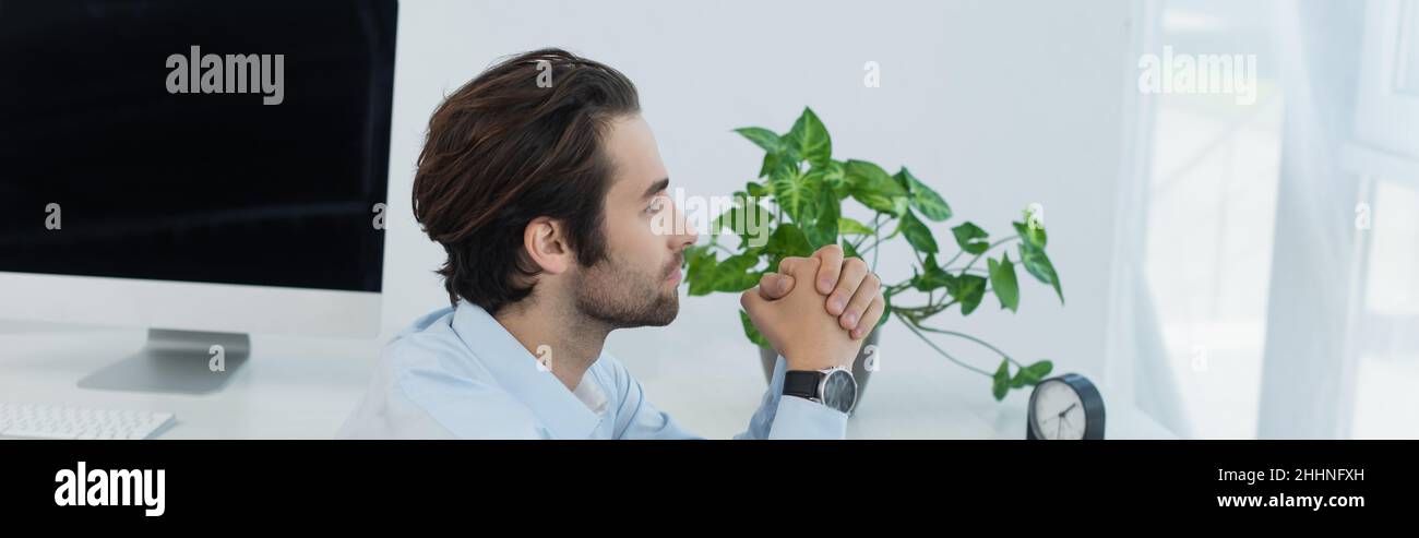 uomo d'affari premuroso con le mani aggrappate che guardano via in ufficio, banner Foto Stock