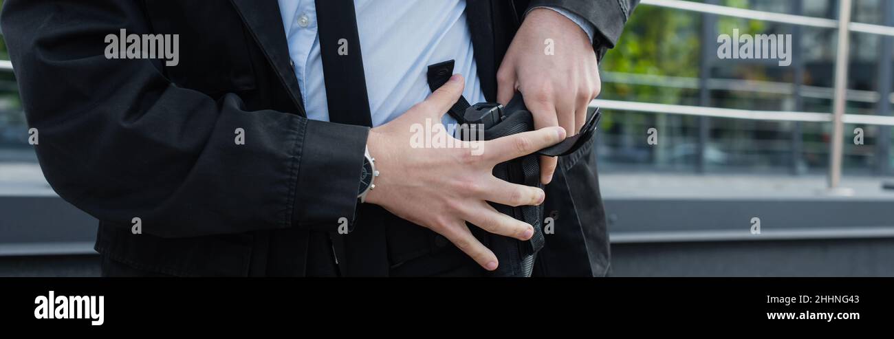vista parziale dell'uomo di sicurezza che prende la pistola fuori dalla custodia all'aperto, banner Foto Stock