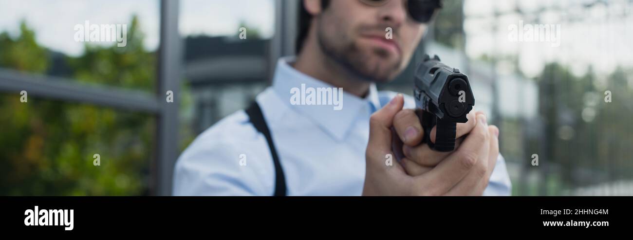 vista parziale di uomo di sicurezza sfocato con pistola all'aperto, banner Foto Stock