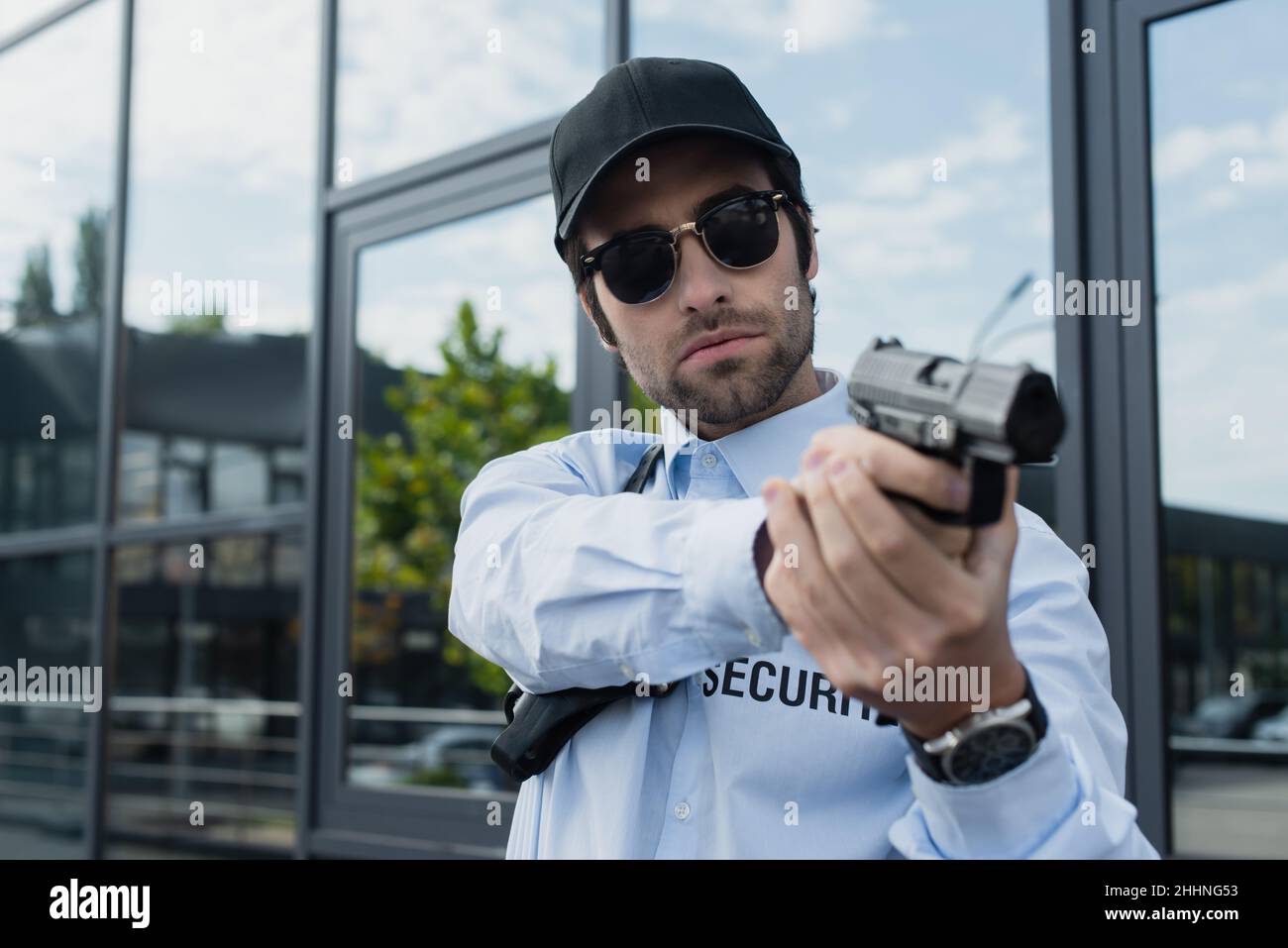 protezione giovane in uniforme, cappuccio nero e occhiali da sole in piedi con pistola all'aperto Foto Stock