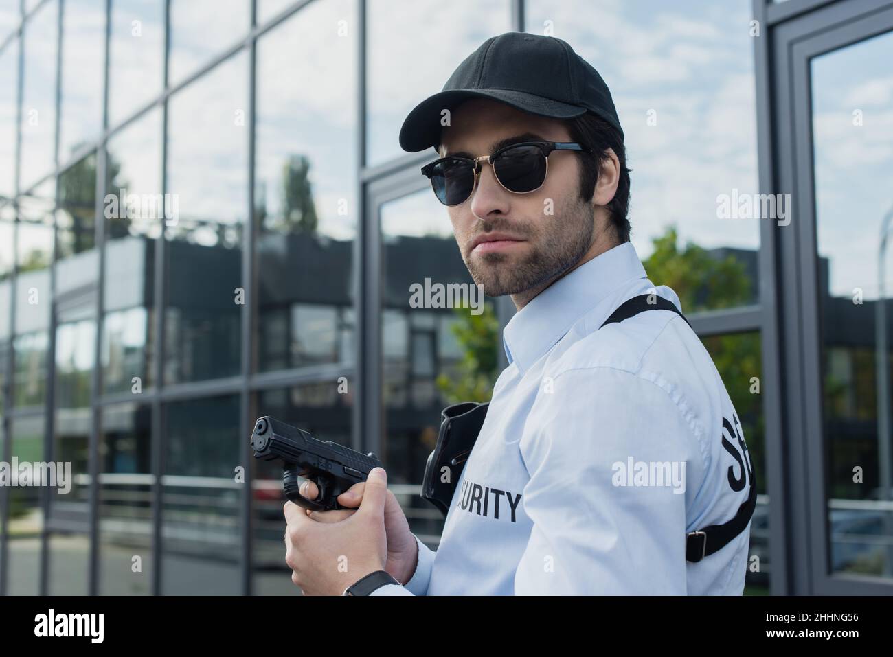 uomo di sicurezza in berretto nero e occhiali da sole che reggono la pistola all'aperto Foto Stock