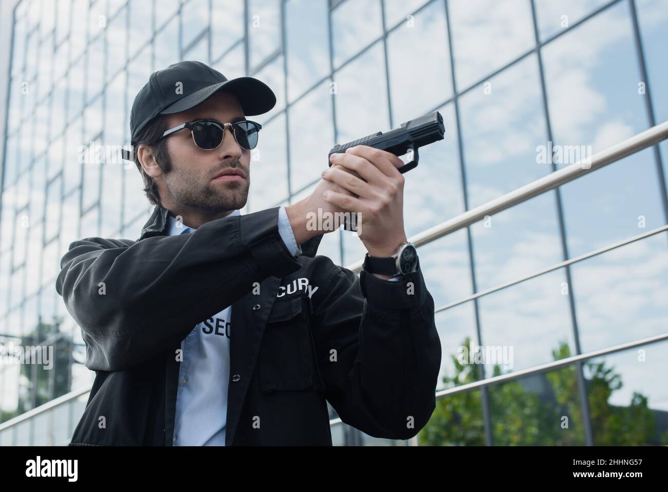 uomo di sicurezza in uniforme nera e occhiali da sole che tengono la pistola mentre si guarda via sulla strada urbana Foto Stock