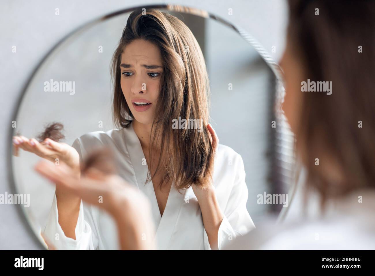 Concetto di hairloss. Preoccupata giovane donna che tiene mazzo di capelli caduti in mano Foto Stock