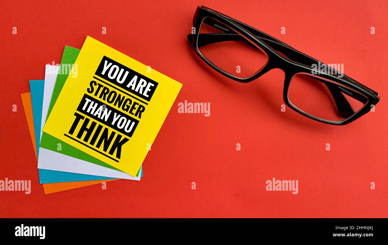 Citazione motivazionale e ispiratrice - sei più forte di quanto pensi. Con nota adesiva, bicchieri e sfondo rosso. Concetto motivazionale. Foto Stock