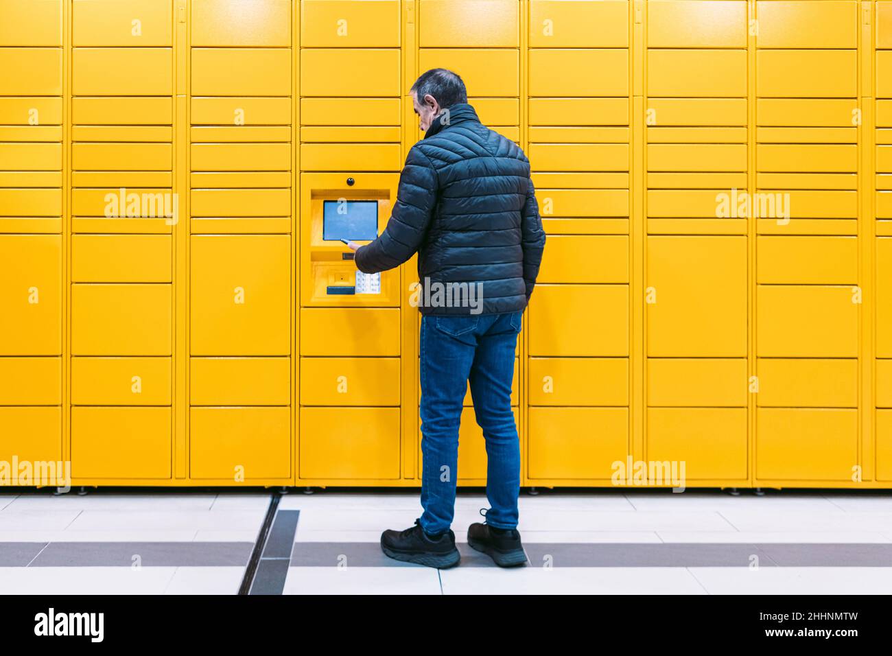 L'uomo da dietro scansiona un codice sul telefono cellulare per ritirare un pacco dall'armadietto giallo. Concetto di messaggistica, confronto online, e-commerce e packag Foto Stock