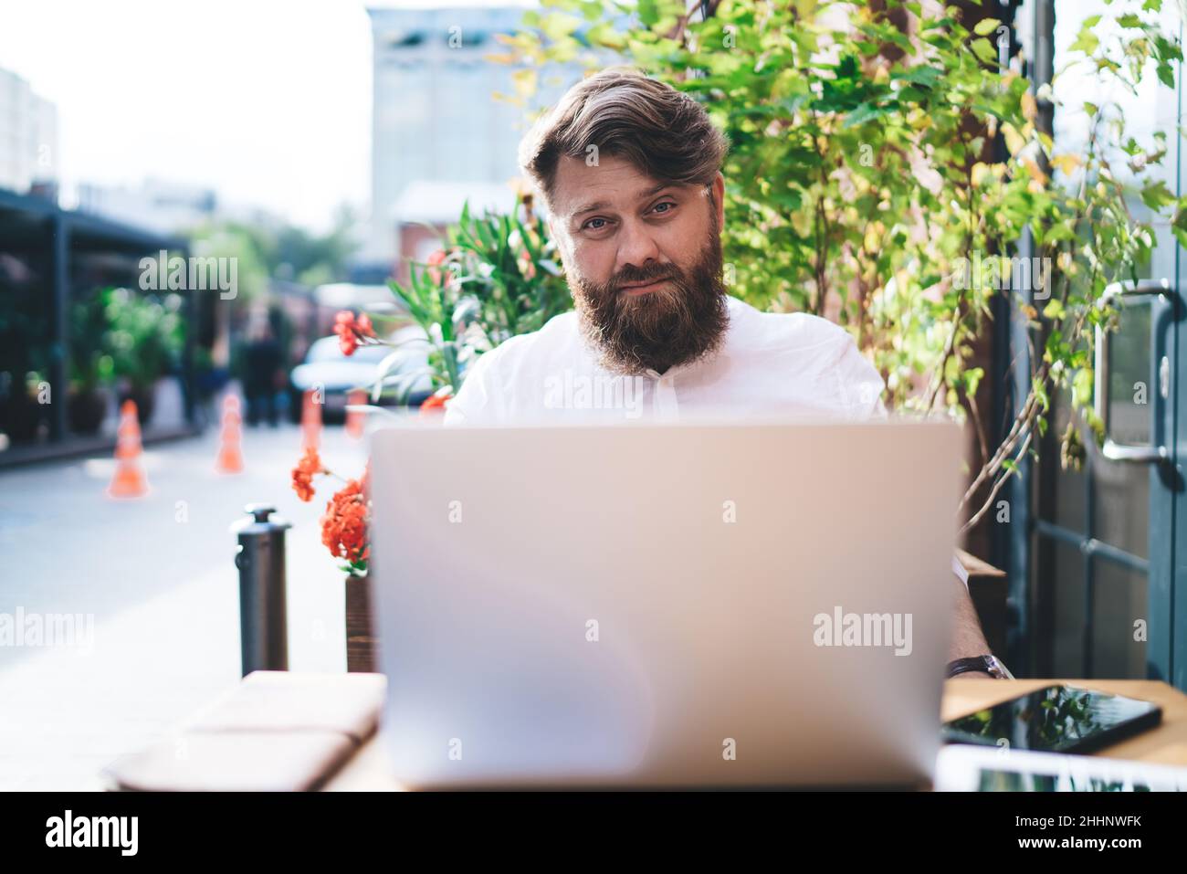 Uomo che lavora su un computer portatile contro piante verdi in un bar Foto Stock