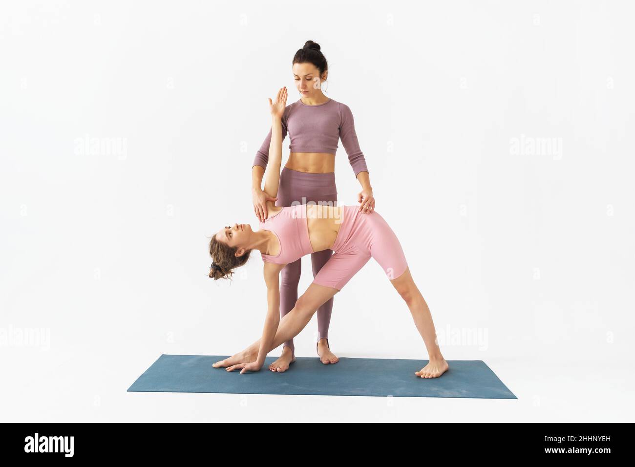 Un addestratore femminile aiuta uno studente a eseguire correttamente l'esercizio di TRIkonasana, posa triangolare, stare su un tappeto su uno sfondo bianco Foto Stock