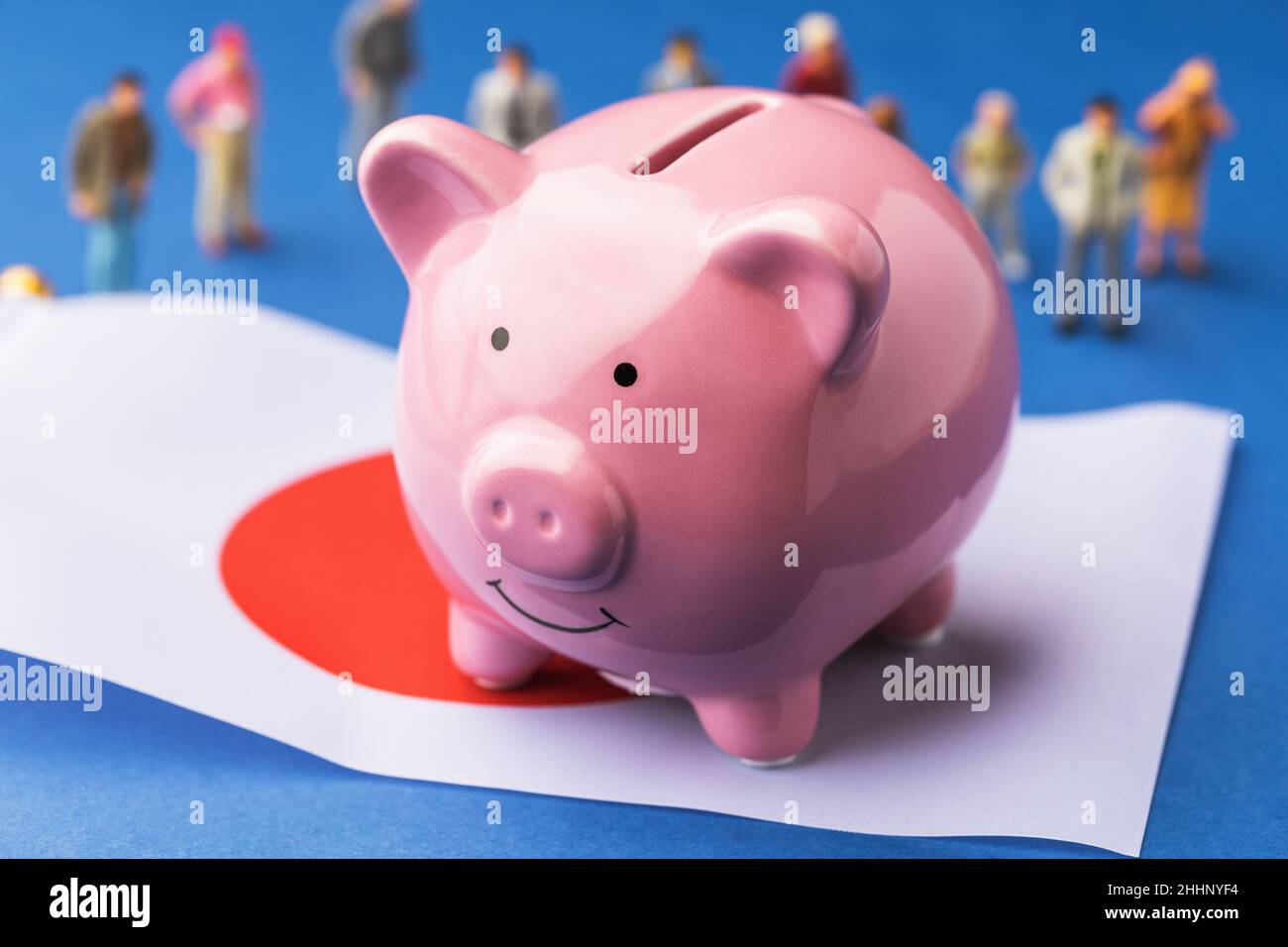 Piggy banca, bandiera e giocattolo persone in plastica su uno sfondo colorato, il concetto del reddito della popolazione del Giappone Foto Stock