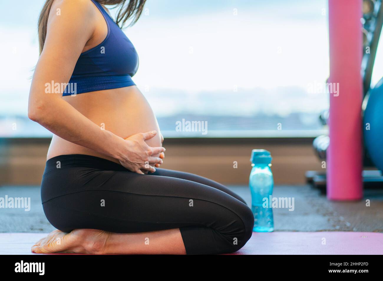 Donna incinta che tocca il ventre mentre si esercita in palestra. Sport durante la gravidanza Foto Stock