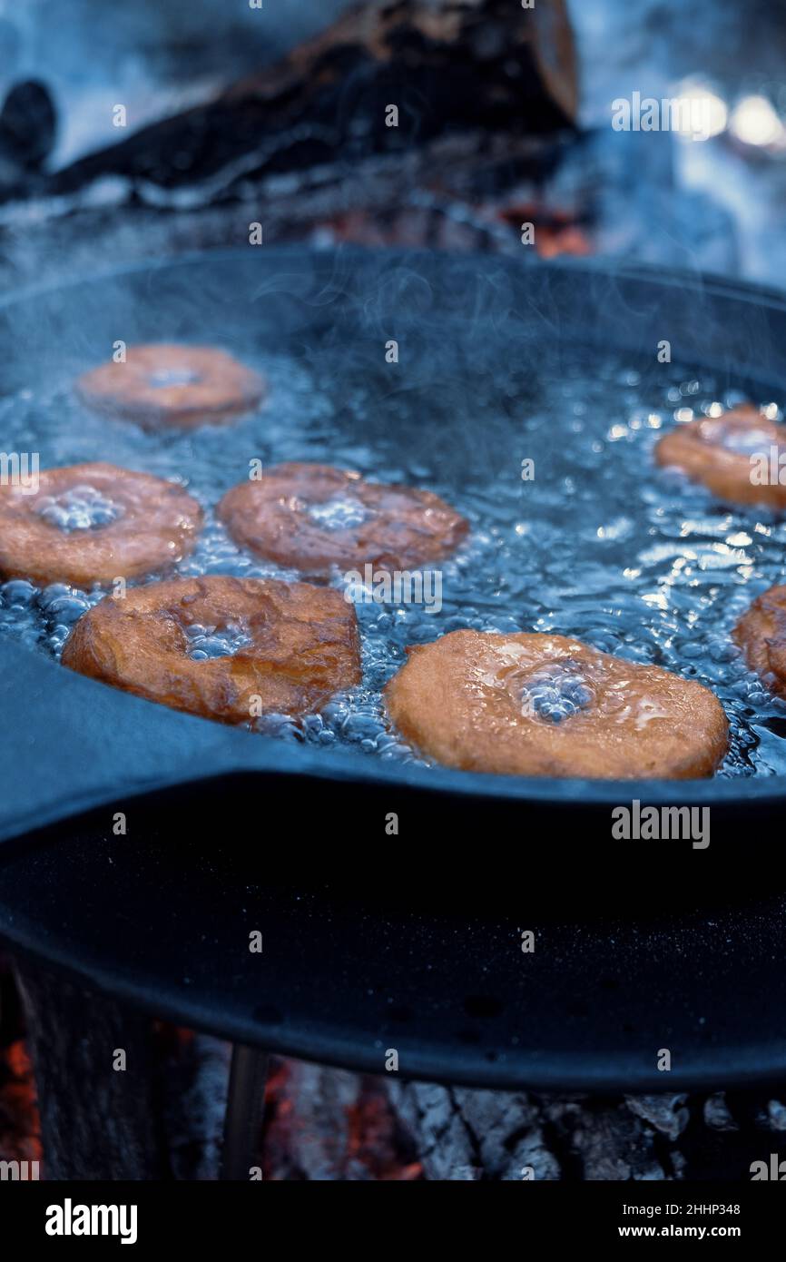 Ciambelle fatte in casa friggere in padella in ghisa all'aperto al campeggio. Foto Stock