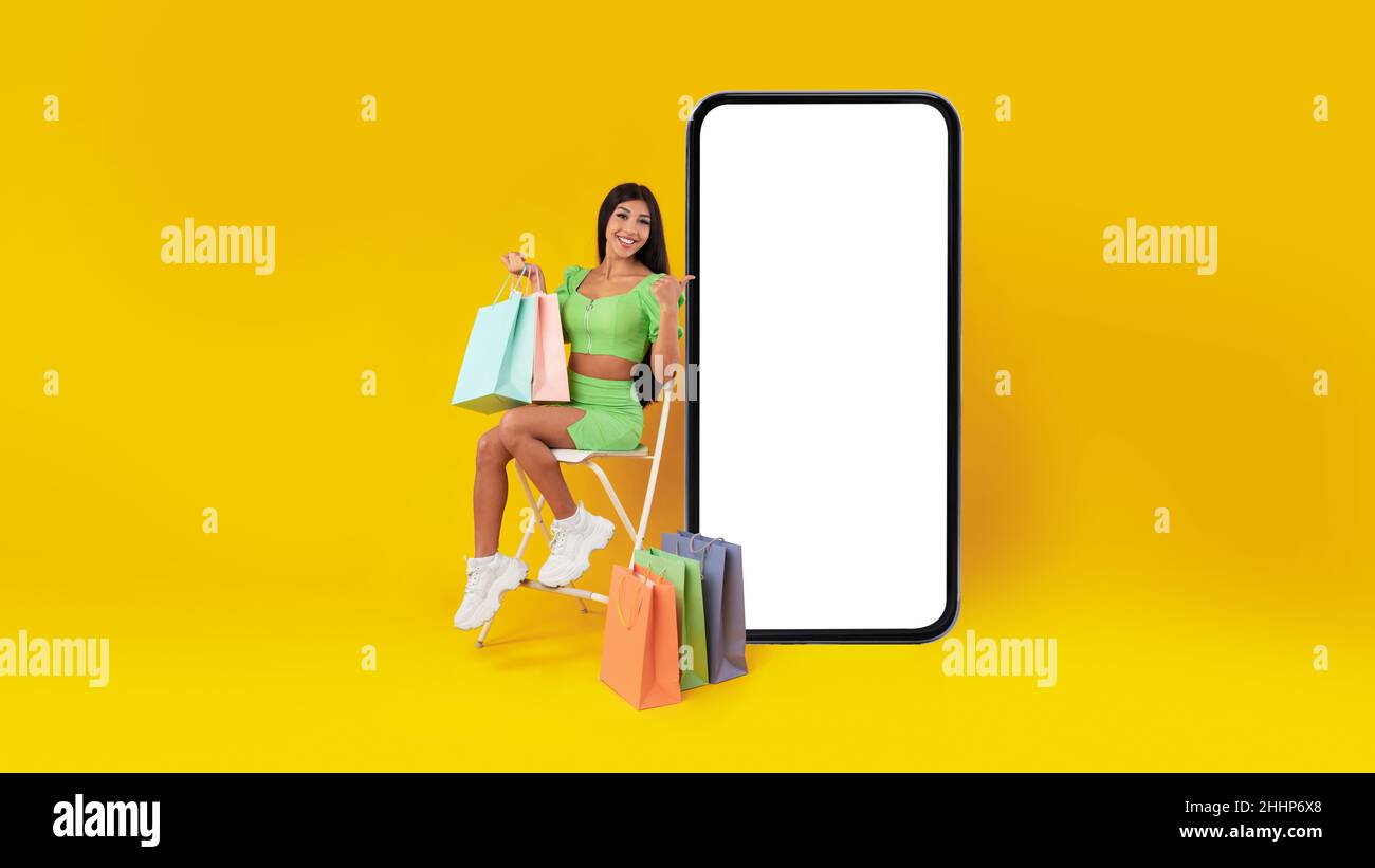 Signora felice con i sacchetti di shopping che puntano allo schermo del telefono mobile Foto Stock