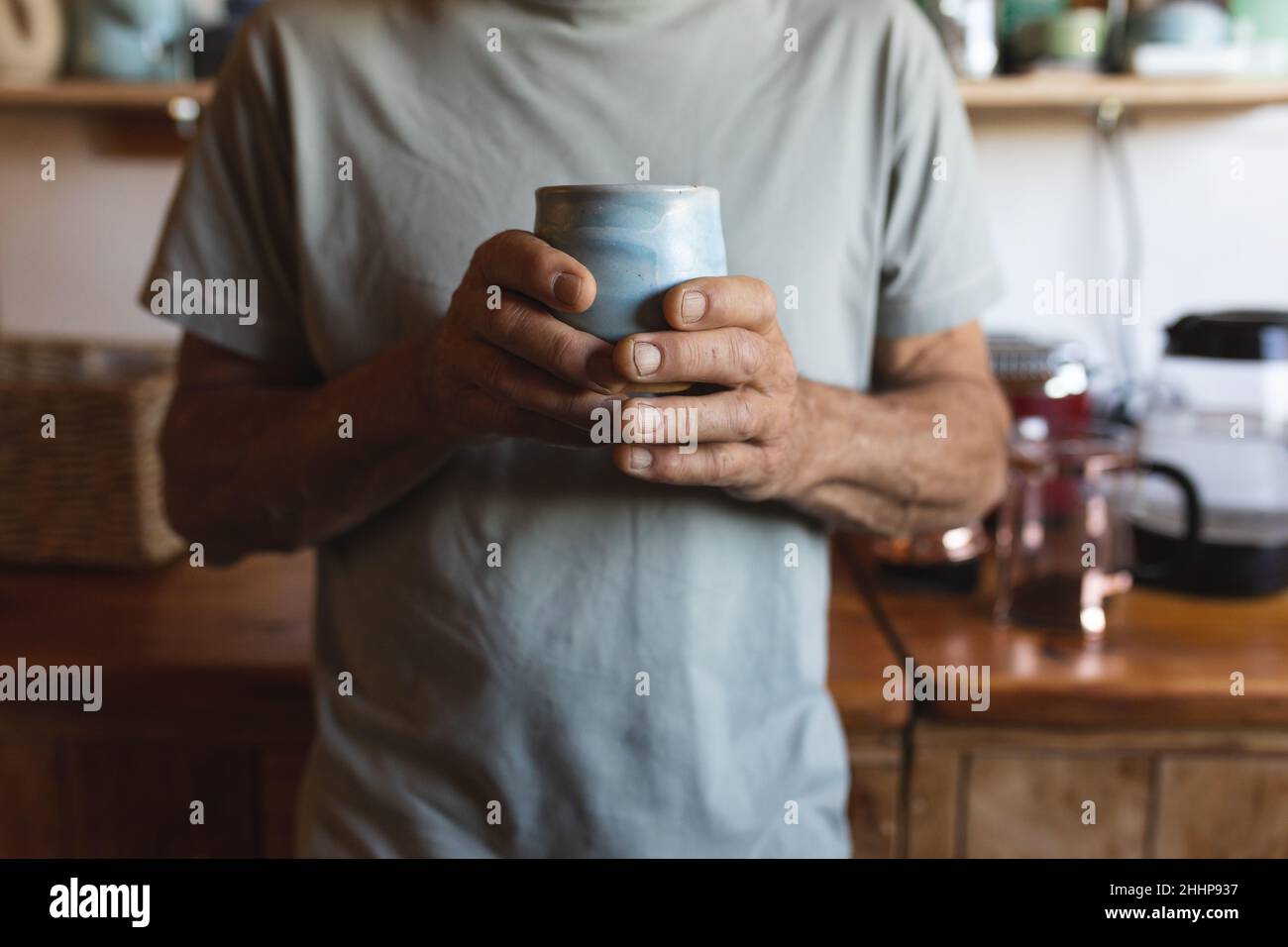 Metà sezione di uomo maturo caucasico che tiene tazza di caffè in cucina alla casa di pannocini. Semplice vivere, stile di vita, bere e rinfresco. Foto Stock
