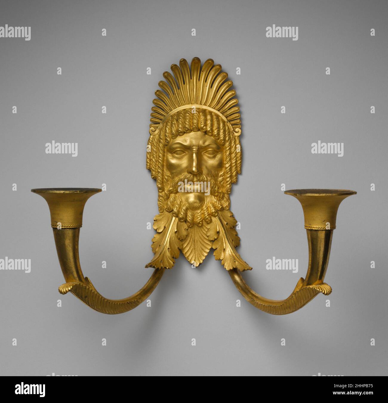 Staffa a parete a due luci ca. 1804–14 attribuita ad Antoine-André Ravrio questa maschera incoronata e barbata di un vecchio uomo porta il numero di inventario del Palais des Tuileries. Uno di un paio, questo muro sconce è stato, secondo l'inventario del 1833, nel pavillon de la Conciergerie nell'appartamento di Emmanuel-Louis-Nicolas Viollet-le-Duc, custode del palazzo e padre del famoso architetto Eugène Emmanuel. Manca un ornamento allungato pendente dal motivo palmette tra i due rami. Questo ornamento è ancora presente su un applique simile, uno di un paio che è stato fornito nel 1808 alla Foto Stock