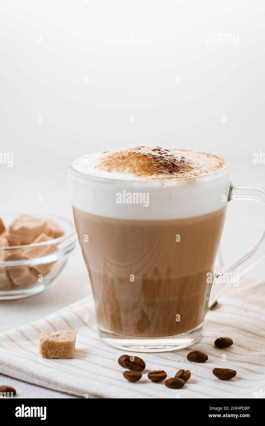 Caffè latte versato a strati con schiuma e un piano croccante al cioccolato su un tavolo da cucina leggero. Immagine verticale con spazio di copia. Foto Stock
