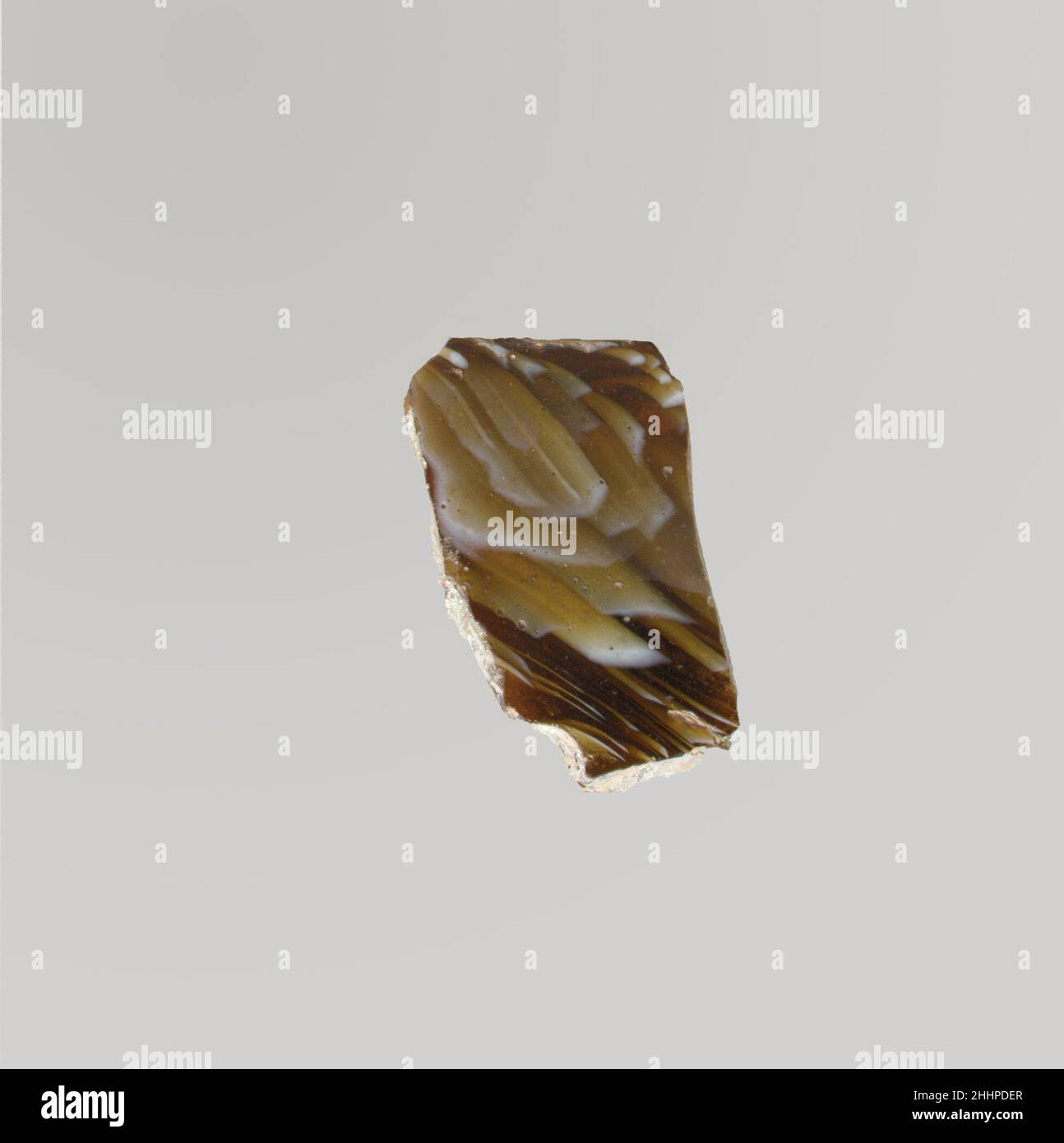 Mosaico di vetro dentellata ciotola frammento fine 1st secolo a.C.–inizio 1st secolo d.C. Roman Rim Fragment.Translucent miele marrone e bianco opaco.bordo verticale arrotondato con labbro esterno leggero; lato rastremato verso il basso.mosaico marmorizzato formato da sezioni di un singolo bastone in marrone macinato con fili e striature bianche irregolari; Sull'esterno, la cresta orizzontale poco profonda sotto il bordo e la nervatura verticale larga con le rientranze di attrezzo attraverso l'interno superiore.lucidato; vaiolatura delle bolle di superficie sull'interno; vaiolatura e iridescente brillante su esterno, bordo e bordi rotti. Vetro mosaico costato ciotola fragm Foto Stock