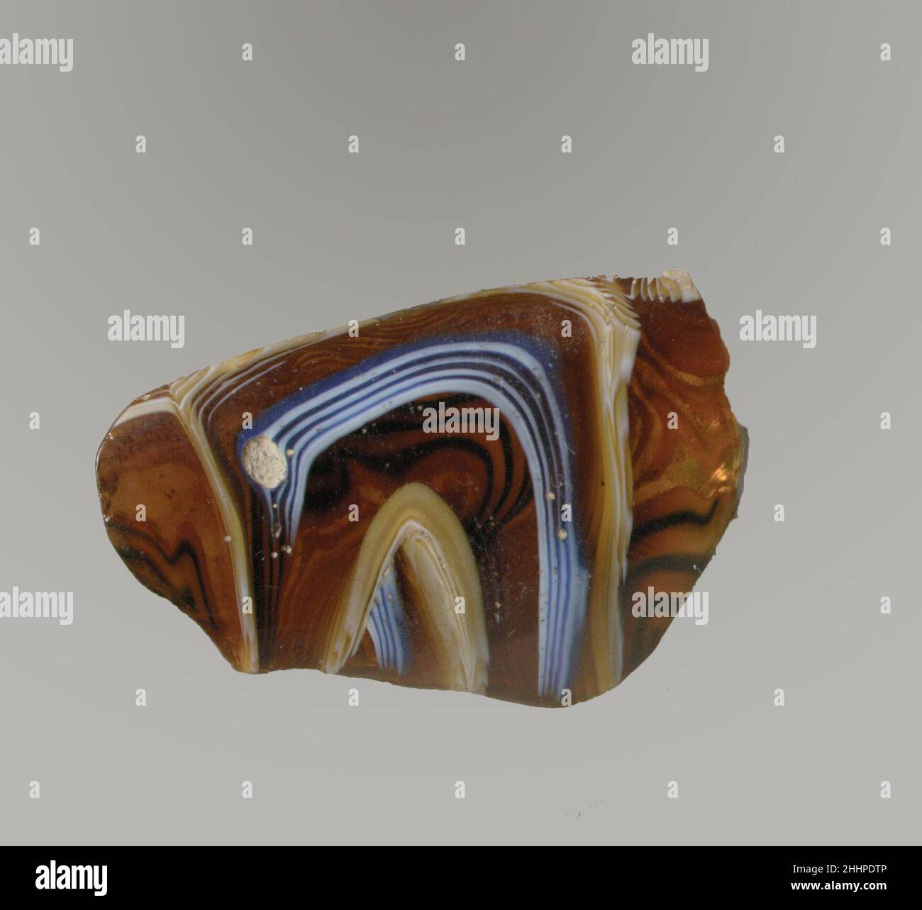 Mosaico di vetro dentellato ciotola frammento fine 1st secolo a.C.–inizio 1st secolo d.C. Roman Rim Fragment.traslucido profondo miele marrone, blu cobalto, e bianco opaco.bordo estricato con labbro arrotondato; Curvatura leggermente convessa rastremata verso il basso.motivo a spirale a mosaico formato da tratti di una o più canne marroni macinati con bande di sottili fili blu e bianchi in linee parallele; all'esterno, parte di un'ampia nervatura verticale, con dentini appiattiti e per utensili ai lati.interno lucido; vaiolatura e intemperatura di bolle di superficie; svergolatura e iridescente cremoso intemperie all'esterno, labbro del bordo, e j Foto Stock