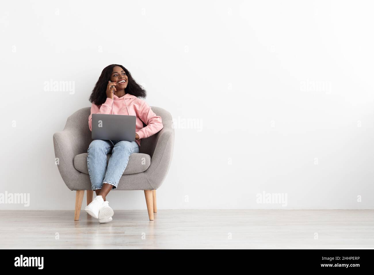 Felice giovane donna nera che ha una conversazione telefonica, utilizzando un portatile Foto Stock