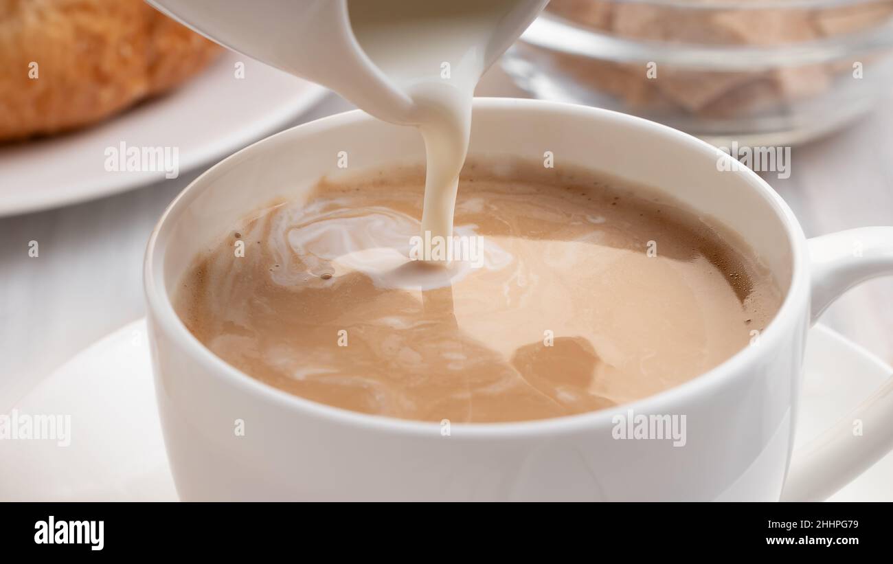Versare il latte o la panna in un caffè appena fatto, primo piano Foto Stock