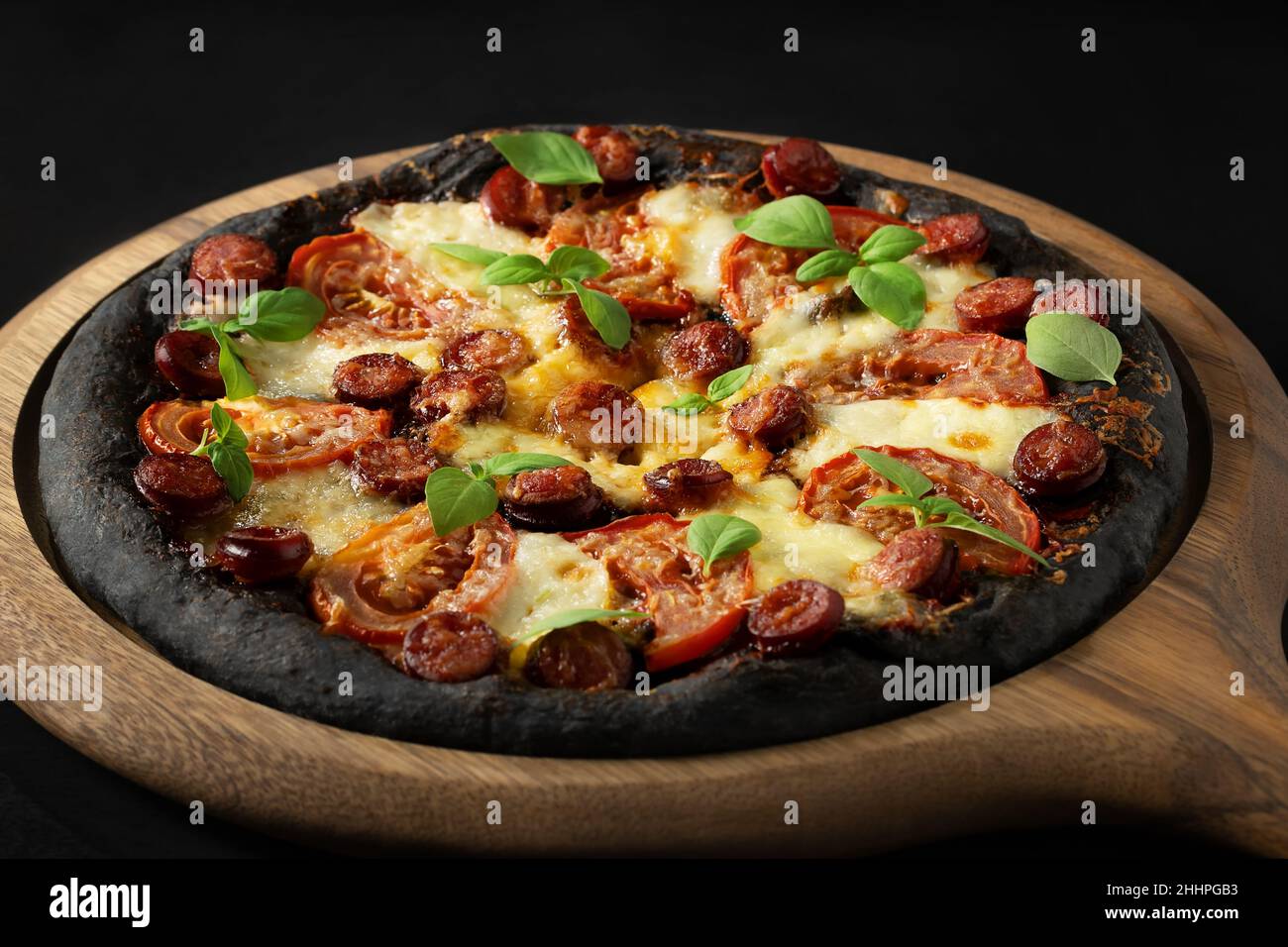 Pizza nera con pomodori, salsicce, mozzarella e basilico. Impasto con polvere di carbone di bambù sano. Foto Stock