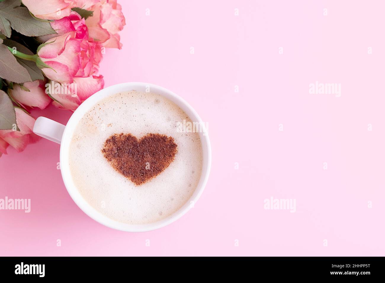 Tazza di caffè con un cuore di cannella su una schiuma di latte con rose rosa su sfondo rosa pastello, spazio copia Foto Stock
