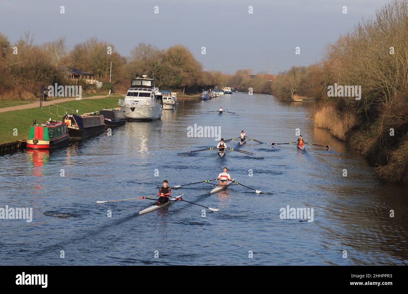 In una mattinata invernale luminosa ma fresca e fresca, un gruppo di vogatori passa accanto alle barche del canale ormeggiate sul Gloucester e sul canale Sharpness al ponte Sellars Foto Stock
