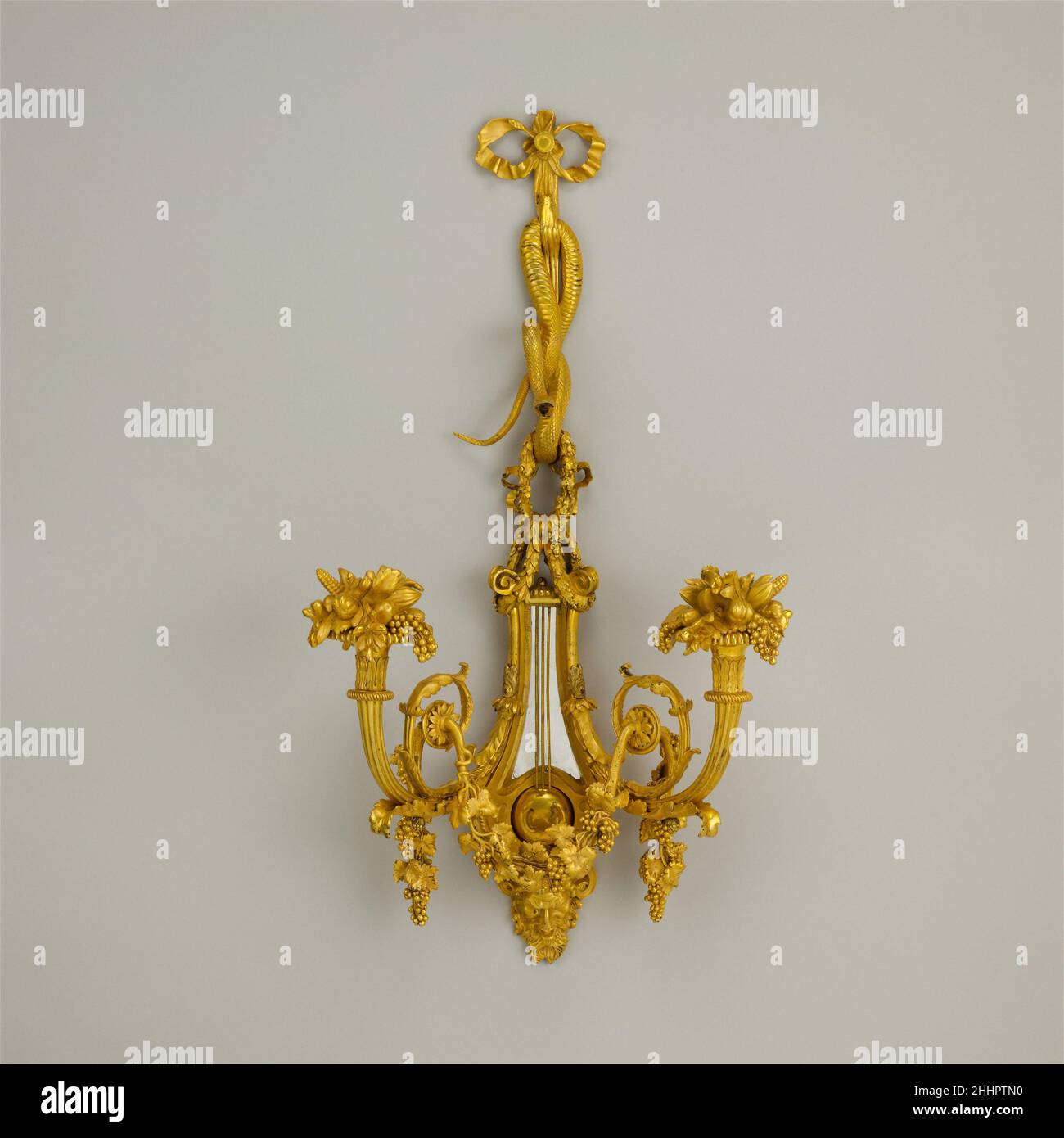 Coppia di staffe da parete a due luci 1780–90 il bronzo dorato francese è stato ampiamente utilizzato per diversi tipi di illuminazione, da candelieri in piedi e candelabri a lampadari e lanterne pendenti. Le luci da parete (bras de lumiere), sono state spesso posizionate su entrambi i lati degli specchi per riflettere il lume di candela. Sospeso da un nastro di bronzo dorato legato in un nodo di prua, un serpente intrecciato contiene una ghirlanda di foglie che sostiene un backplate a forma di lira, mentre un flauto in padella, il tambourine e il thirso sono sospesi su un nastro al di sotto di una maschera di satiro. La decorazione allude chiaramente a Bacco, il dio romano del vino e re Foto Stock