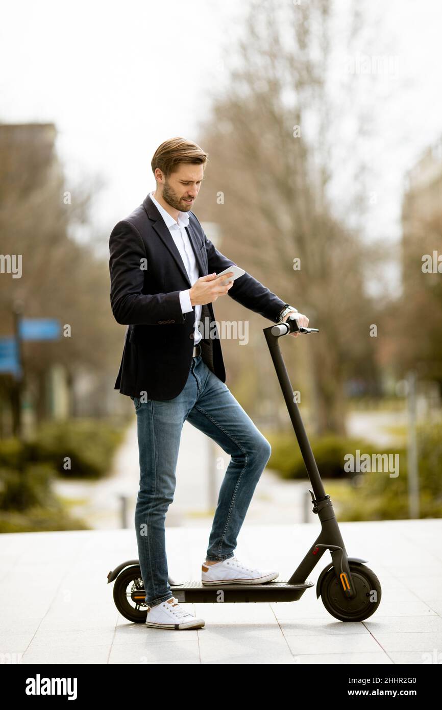 Bel giovane uomo d'affari che usa il telefono cellulare su scooter elettrico Foto Stock