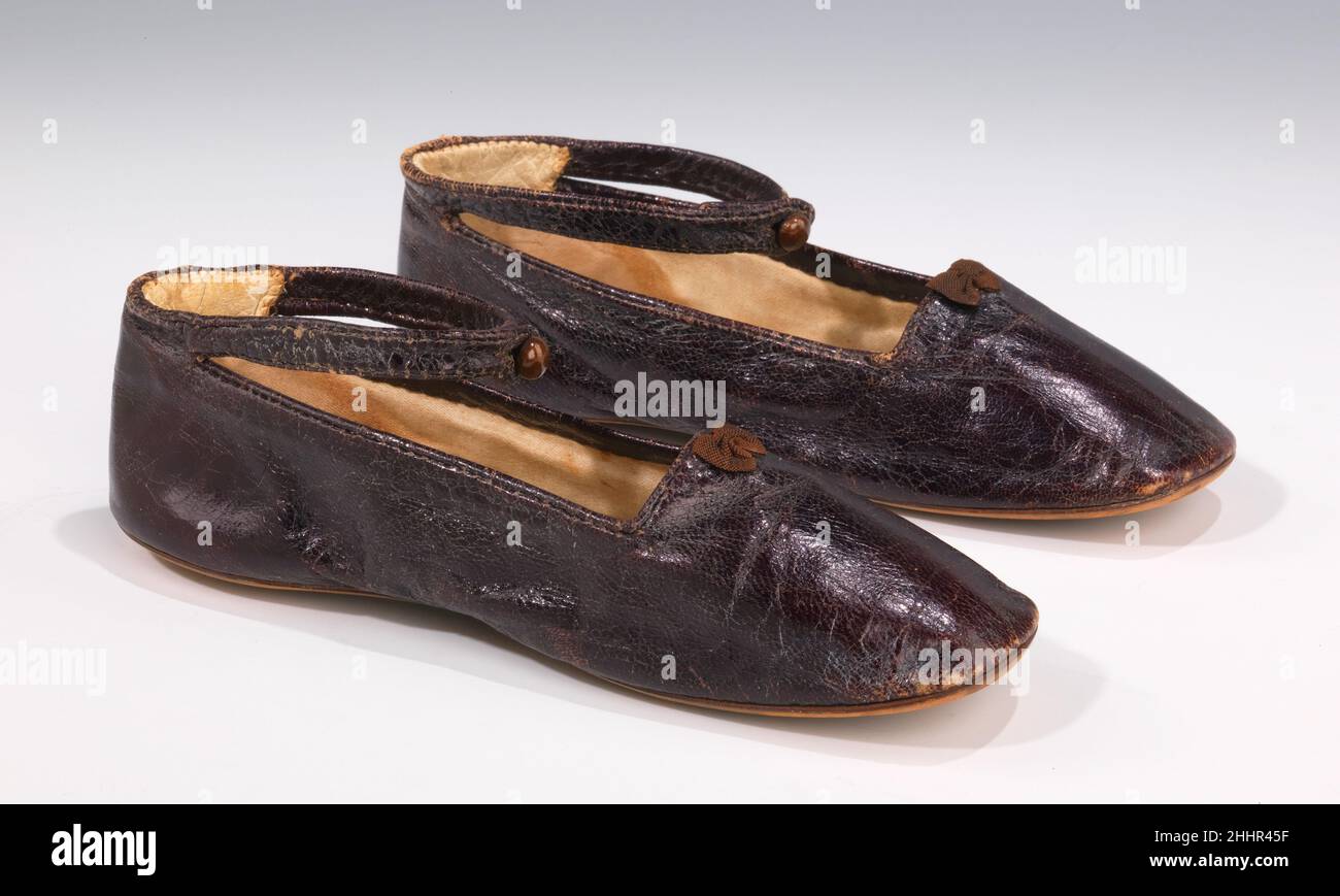 Scarpe 1850–69 europeo queste eleganti pantofole sono essenzialmente una versione miniaturizzata di uno stile adulto, ma includono una caviglia-cinghia integrale, rendendole così adatte per un bambino. La piccola prua, le raffinate tubature in pelle e il bottone metallizzato sono elementi piacevoli che mostrano l'attenzione al dettaglio. Il bambino di bronzo è stato usato ampiamente durante la seconda metà del 19th secolo per le scarpe da donna. Il caratteristico colore marrone violaceo con lucentezza metallica o iridescente è stato prodotto tintando la pelle con cocineale, un colorante rosso prodotto dalla frantumazione dei corpi essiccati dell'insetto Dactylopio coccus Foto Stock