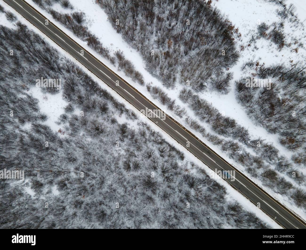 Vista aerea dall'alto verso il basso ad angolo alto, immagine drone su strada attraverso gli alberi e la foresta in catena montuosa coperto con Neve bianca nella giornata invernale vicino a Knjazevac Foto Stock