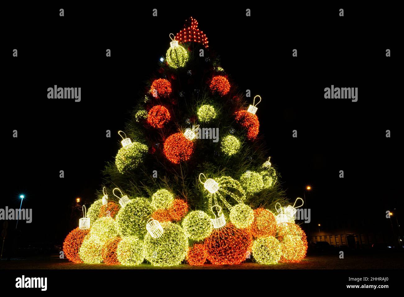 Un albero di Natale in una piazza della città di notte, decorato con grandi palline colorate Foto Stock