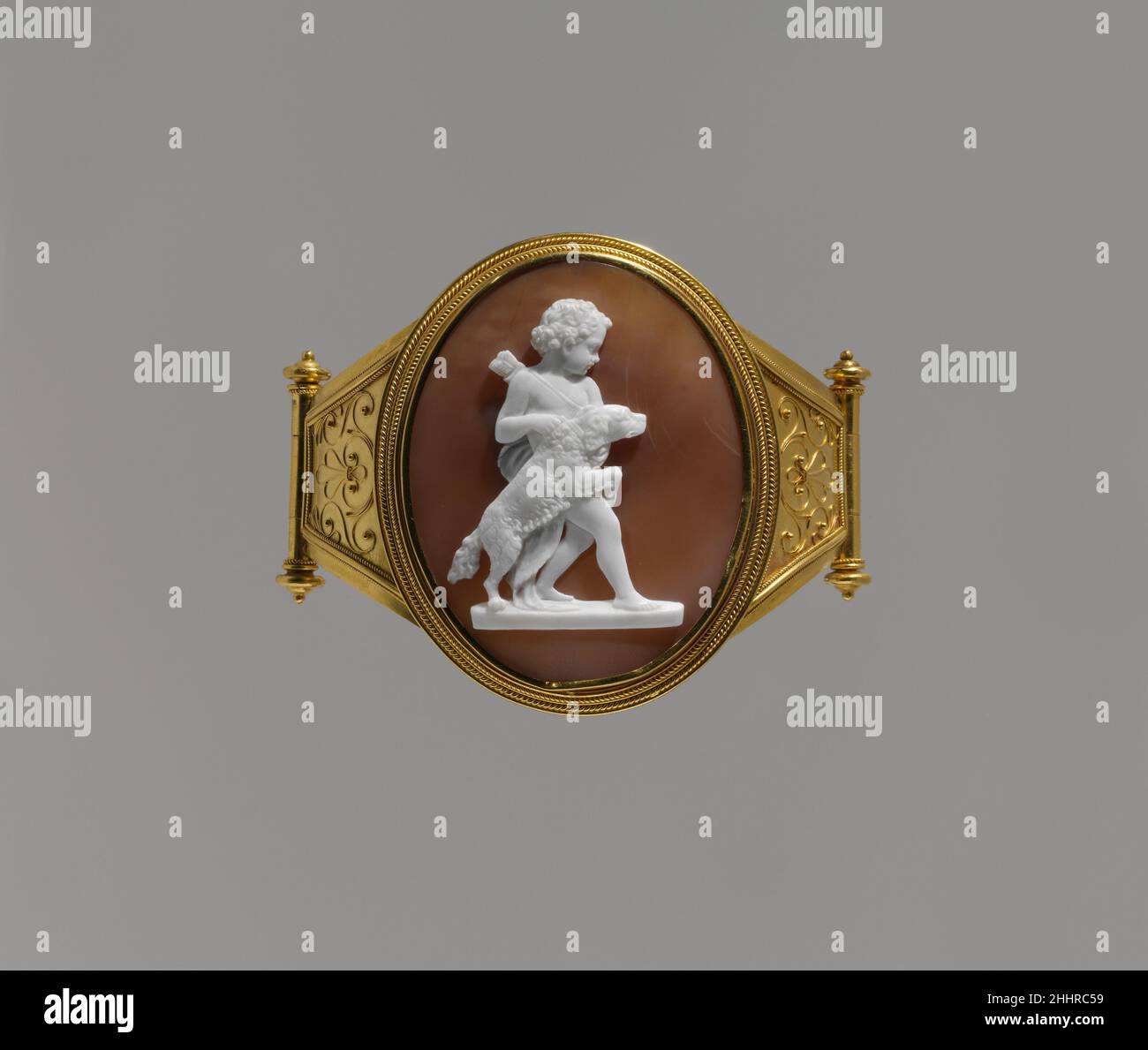Cupido con un cane 1860–70 Luigi Saulini Luigi Saulini era un carver in pietra di grande destrezza. Più frequentemente produsse cameo di conchiglia, per i quali addebitò un decimo del prezzo. Gran parte della sua produzione era basata su statuario dai suoi contemporanei. Il modello qui era un gruppo marmoreo ancora non identificato nel tondo (indicato dal plinto in basso). Il braccialetto, insieme ad un altro che mostra un circo di microscopia di ragazze contadine italiane, è stato lasciato in eredità da una coloratissima Irishwoman, Maria Morgan, la cui conoscenza dei cavalli ha portato il re Vittorio Emanuele d'Italia ad affidarla al suo stab Foto Stock