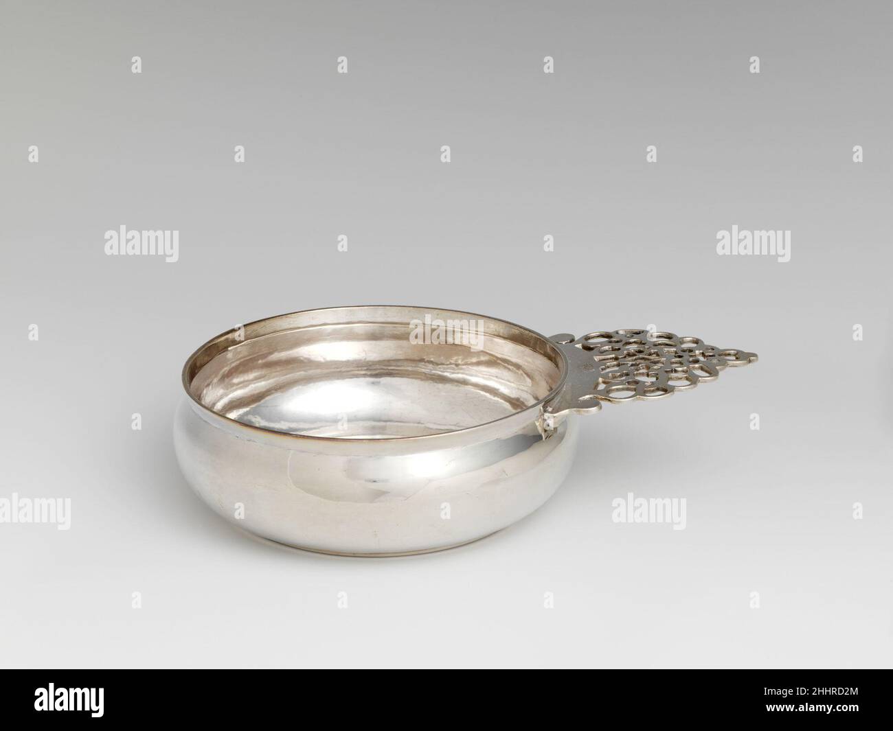 Porringer 1700–1725 Peter Van Dyck le maniglie dei portinger di New York mostrano spesso il motivo pierced lacy visto qui, un disegno simmetrico elaborato che incorpora i motivi della croce e del cuore alla punta. Peter Van Dyck ha fatto diversi esempi simili, ma i porringer con questo tipo di manico sono stati prodotti anche da altri produttori di New York. Con il suo matrimonio nel 1711 con Rachel le Roux, Van Dyck era legato alla famiglia le Roux degli argentini francesi Huguenot, e contava tra i suoi patroni alcuni dei cittadini coloniali più ricchi e prominenti di New York, come i Livingstons e gli Schuylers. U Foto Stock