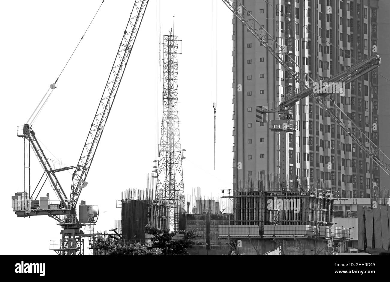 Immagine monocromatica delle gru in cantiere con una torre di telecomunicazione sullo sfondo Foto Stock