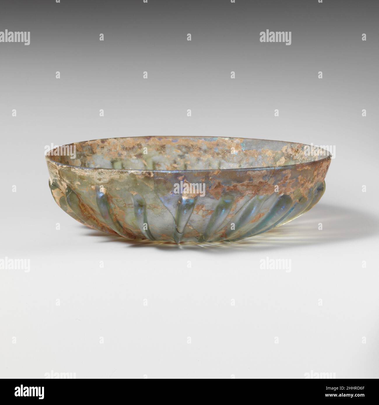 Vetro costato ciotola fine 1st secolo a.C.–metà 1st secolo d.C. romano traslucido blu pallido verde.bordo arrotondato liscio; lati curvati verso leggermente concavi, basso irregolare.sul esterno, ventidue nervature prominenti con sommità arrotondate e rastremati verso il basso, quasi toccando a center.Complete; rotto e riparato intorno ad un lato; pochissime bolle; Scolorimento, vaiolatura leggera, e numerose macchie di iridescente cremoso Weathering.Rotary macinatura segni all'interno del fondo. Vaschetta in vetro a coste 239874 Foto Stock