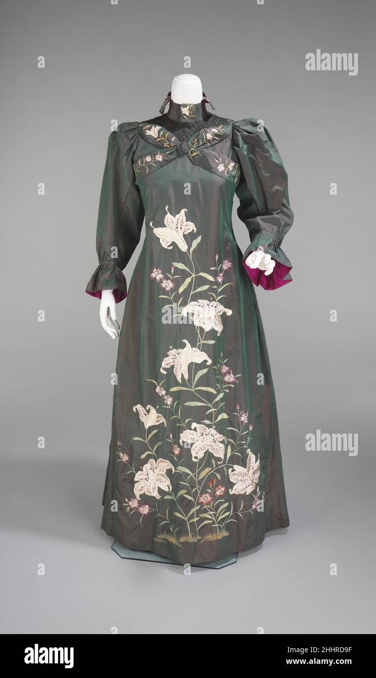 Abito da tè 1898–1901 britannico Una donna indossava una teagown per ricevere ospiti nella propria casa nel tardo 19th e all'inizio dei 20th secoli. Questi indumenti erano molto meno formali e strutturati che indossarono tipicamente di giorno o di sera, e di conseguenza, a volte mostrano ispirazioni più creative o insolite, come forme storiche o non occidentali di abbigliamento. Questo esempio è una bella teagown fatta e decorata, che mostra l'influenza sia del kimonos giapponese ricamato e 18th secolo accappatoi à la franaise. Imbottitura interna destinata a fornire calore e la scelta deliberata di un rivestimento magenta che raccoglie il Foto Stock