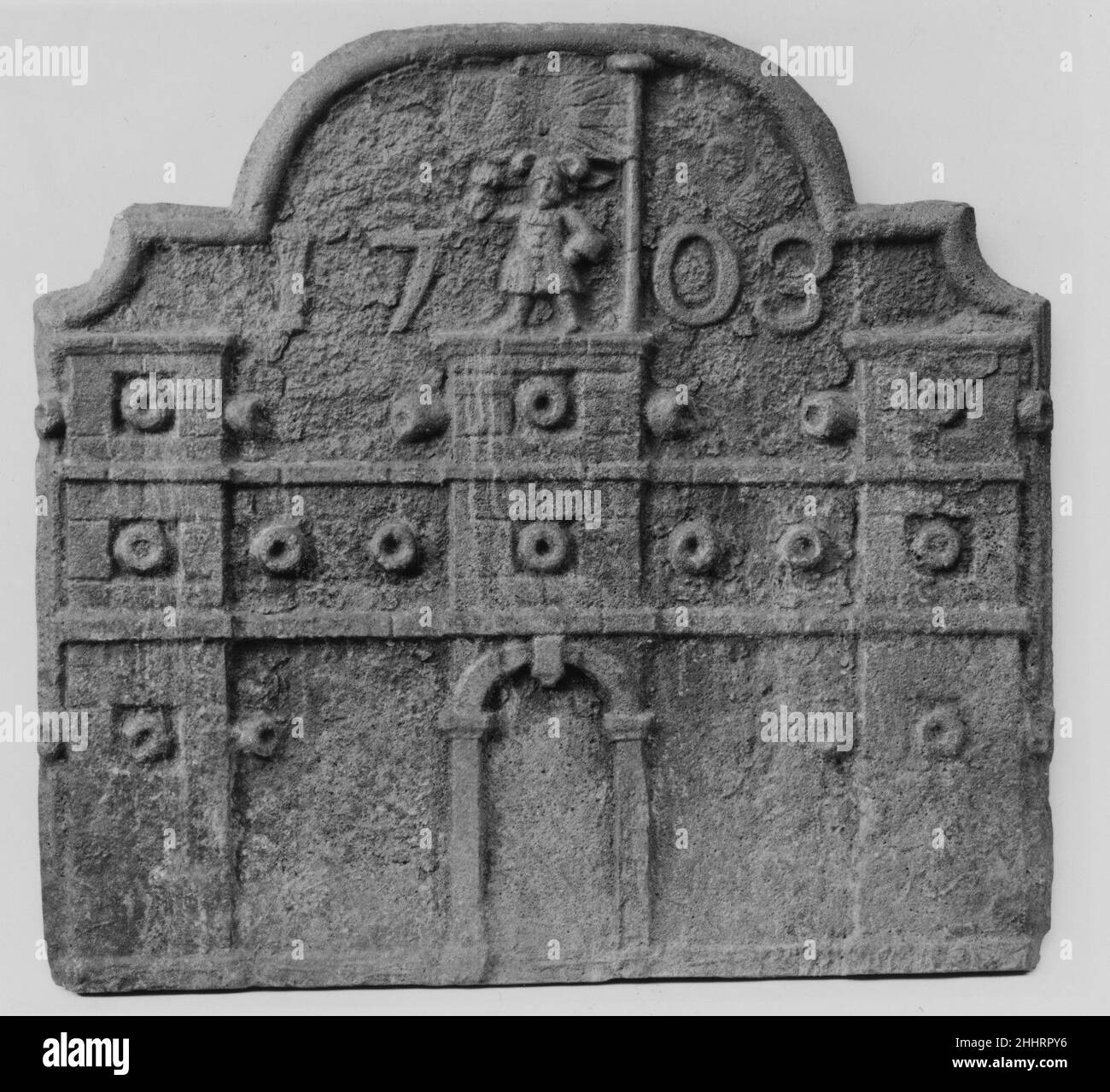 Fireback 1703 American Cast Iron Firebacks servì il duplice scopo di riflettere il calore di un fuoco di nuovo in una stanza e proteggere mattoni vulnerabili e intonaco sulla parete posteriore di un camino. Colto con l'immagine di una fortezza di pietra, inondati di cannoni e una figura dominante in cima a un bastione, battenti una bandiera britannica, presenta anche la data "1703", probabilmente l'anno della sua fabbricazione.. Fireback. Americano. 1703. Ghisa. Possibilmente fabbricato a Newport, Rhode Island, Stati Uniti Foto Stock