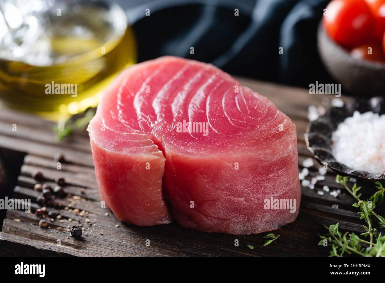 Bistecca di tonno rosa crudo e spezie su tagliere di legno, vista da primo piano Foto Stock