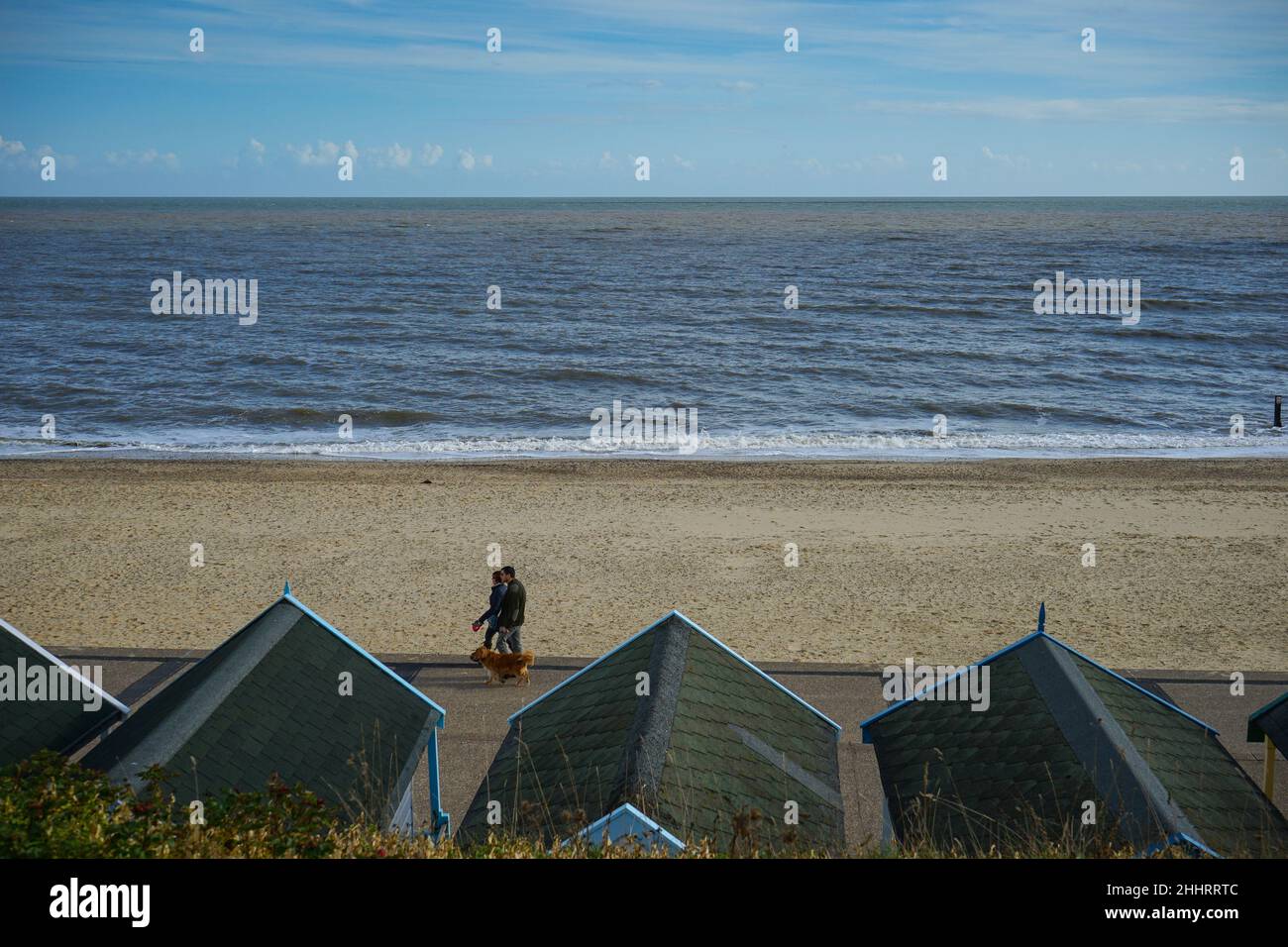 Coppia camminando lungo un fronte mare inglese con capanne in primo piano Foto Stock