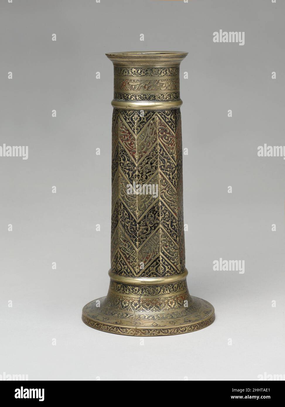 Lampada incisa Stand con modello Chevron datato A.H. 986/ A.D. 1578–79 la poesia inscritta attorno a questo supporto di lampada esprime mistici sentimenti Sufi. I versi lirici del Bustan (Orchard) di SA'dai sono posti in tre registri a forma di zig-zag che coprono il pozzo: Ricordo una notte come i miei occhi non dormirebbero ho sentito una falena parlare con una candela. [Ha detto la falena:] 'perché sono un amante, è [solo] giusto che io debba bruciare.[ma] perché devi piangere e bruciare te stesso?' Ascolta gli esperti che illuminano la storia di questa opera d'arte Ascolta Riproduci o pausa #6725. Stativo per lampada inciso con motivo a freccia, P Foto Stock