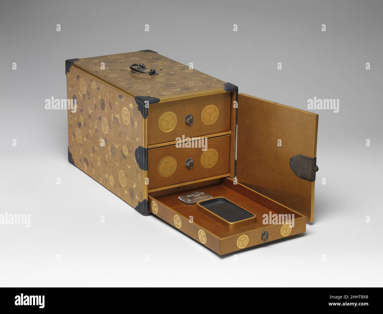 Mobile Writing Cabinet with Tokugawa Family creste, Chrysanthemums, and Foliage Scrolls fine 17th secolo Kōami School questa scatola di scrittura portatile ha tre cassetti; i due superiori sono per carta e documenti, mentre quello inferiore contiene la pietra a inchiostro, gocciolatore d'acqua, e pennelli. L’armadio è finemente decorato con maki-e di altissima qualità (“quadri cosparsi”). È stato prodotto per la famiglia Tokugawa in uno dei loro laboratori ufficiali maki-e, probabilmente quello della famiglia Kōami. I fiori di crisantemo sono raffigurati quasi individualmente, ciascuno eseguito in una tonalità o mak differente Foto Stock