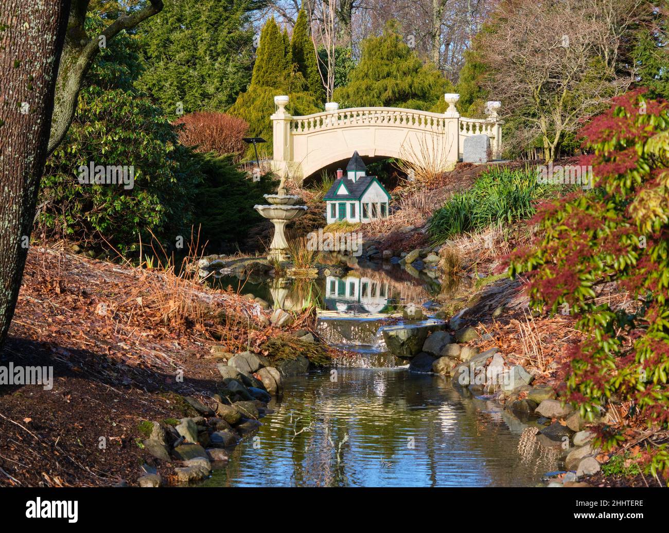 All'interno dei giardini pubblici di Halifax, ponte vittoriano sopra lo stagno con fontana e casa di bambole in un giorno d'autunno Foto Stock