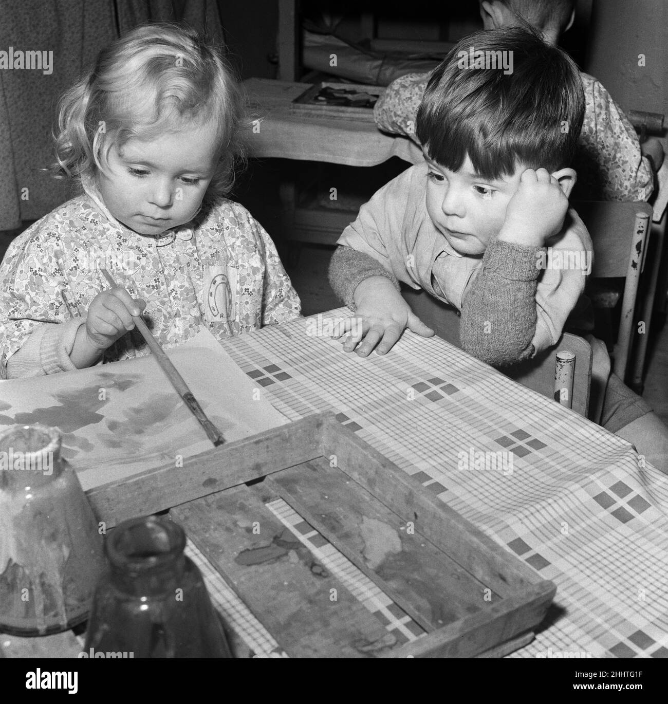 Rosemary Street Nursery School, Bristol. Nella foto, Myra Edbrook di 3 anni dipinge mentre Roger White di 2 e 1/2 anni tiene d'occhio il soggetto. 20th aprile 1954. Foto Stock