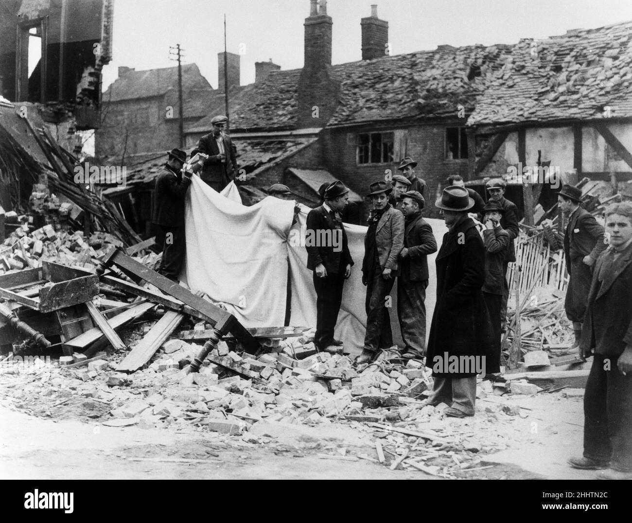 I soccorritori hanno visto qui tenere fogli per nascondere il recupero di corpi da una casa bombata vicino al centro di Coventry. 15th novembre 1940. il raid fu eseguito da 515 bombardieri tedeschi, due terzi da Luftflotte 3 e il resto dai pathfinder di Kampfgruppe 100. L'attacco, denominato in codice operazione Mondlicht Sonaten (Moonlight Sonata), era destinato a distruggere le fabbriche e le infrastrutture industriali di Coventry, anche se era chiaro che i danni al resto della città, compresi monumenti e aree residenziali, sarebbero considerevoli. Foto Stock