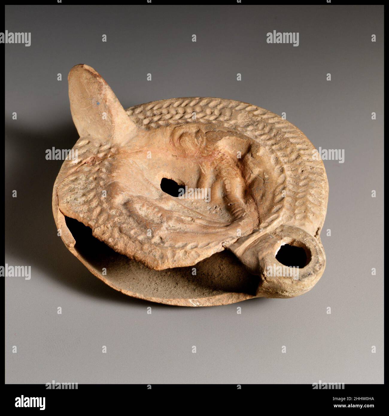 Lampada ad olio di terracotta fine 2nd a 3rd secolo d.C. romana, cipriota Loeschcke tipo 8. Impugnatura non forata. Realizzato in stampo. Discus: Due gladiatori: A sinistra, uno in piedi, rivolto a destra, con una spada al suo fianco nella mano destra e un lungo tridente alla sua sinistra; a destra, l'altro cadendo all'indietro, rivolto verso sinistra, indossando un grande casco, tenendo una piccola spada nella mano destra davanti a lui e il suo scudo sotto a sinistra. Sulla spalla: Doppia corona d'aringa. Su base concava con anello di base, in grandi lettere incise greche: ?PMI/ANO. Rotto lungo il lato sinistro con bordo di spalla mancante e un grande foro in Foto Stock