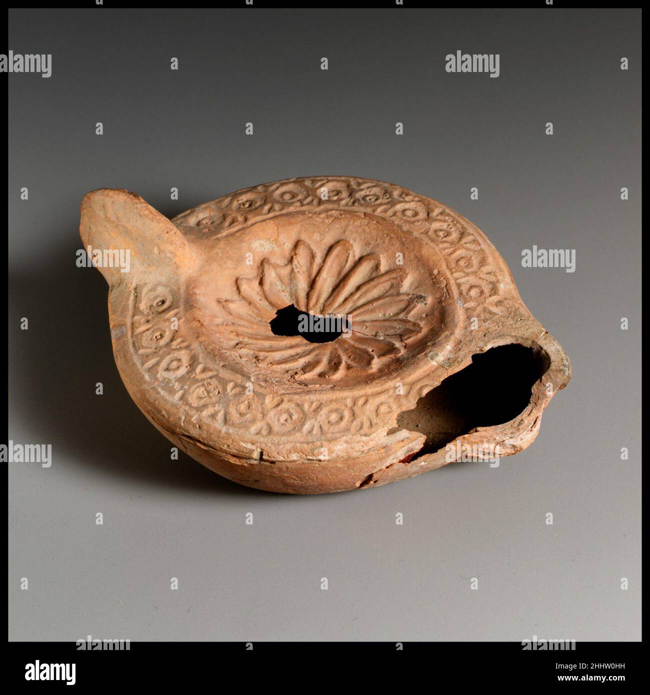 Lampada ad olio di terracotta fine 3rd secolo d.C. romana, Cypriot Loeschcke tipo 8. Impugnatura non forata. Realizzato in stampo. Disco; rosetta con petali cavi sovrapposti attorno al foro centrale di riempimento. Spalla: Motivo a catena di cerchi e punti all'interno di due linee incise. Su una base leggermente concava, scritta in greco: C?PI?/WNOC. Rotto intorno all'ugello, parzialmente riparato ma manca il lato sinistro; piccolo foro che si estende verso l'impugnatura dal foro di riempimento. Lampada ad olio di terracotta. Romano, cipriota. Fine 3rd secolo d.C.. Terracotta. Tardo imperiale. Terracotte Foto Stock