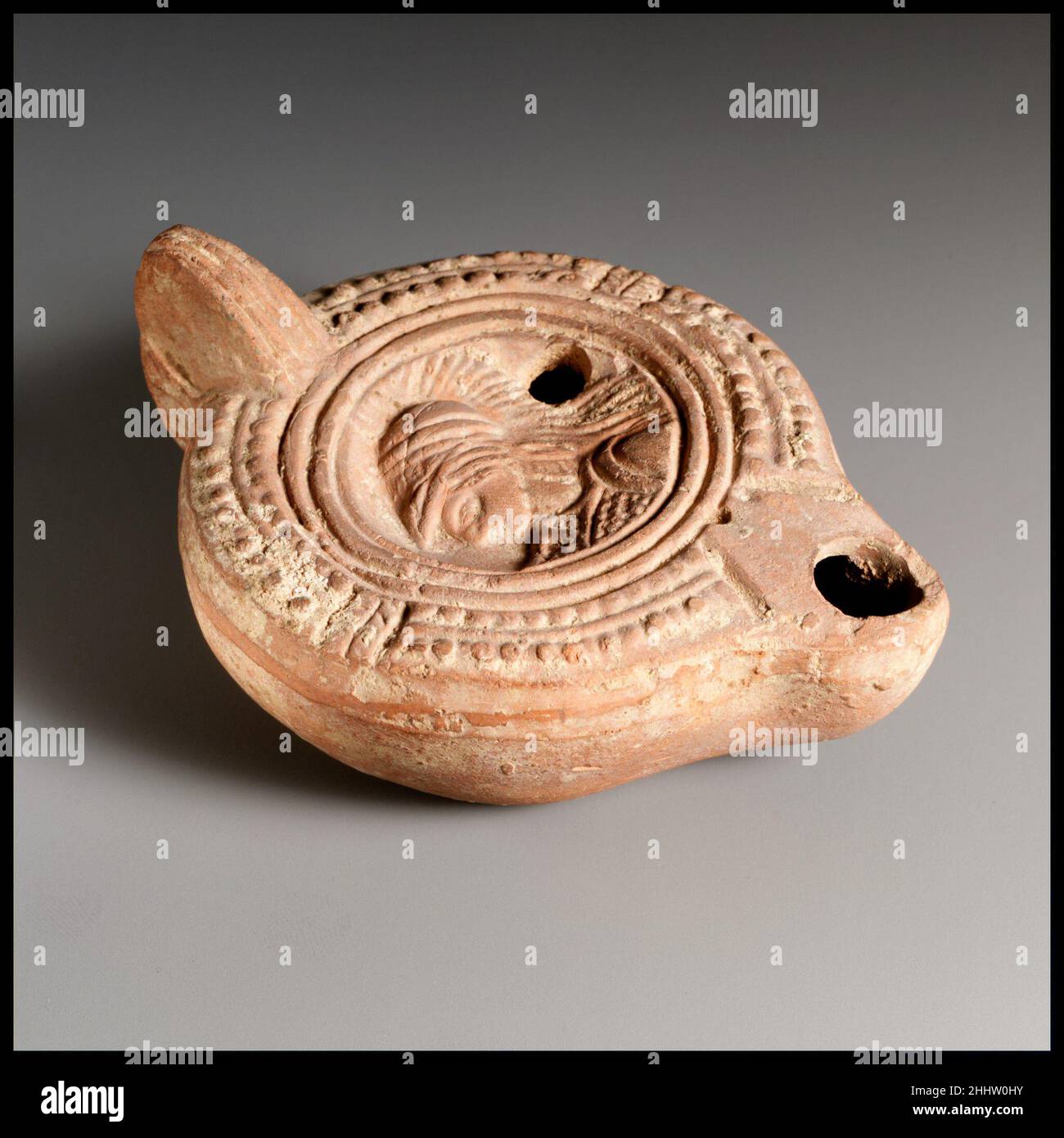 Lampada ad olio di terracotta 3rd–inizio 4th secolo d.C. Broneer romano tipo 28. Realizzato in stampo, con manico non forato. Disco: Busto di Atena helmeted, rivolto verso sinistra; un unico foro di riempimento a destra; intorno al disco, una banda di due linee concentriche in rilievo, circondata. Spalla: Corona stilizzata interrotta da pannelli laterali. Un piccolo foro sul retro dell'ugello. Linee incise che corrono lungo la lunghezza del manico. All'interno di un anello di base impresso, una base piatta impressa con le lettere greche EY.intact.The base del manico sembra essere stato fatto con la lampada nello stampo; la parte superiore e anteriore è stato poi careles Foto Stock
