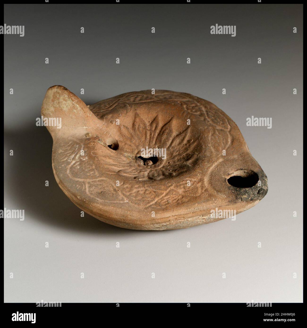 Lampada ad olio di terracotta ca. A.D. 200–350 Roman, Cypriot Loeschcke tipo 8. Manico grande non forato. Realizzato in stampo. Disco; rosetta con petali appuntiti e irradianti attorno al foro centrale di riempimento; un secondo foro di riempimento davanti al manico. Su spalla larga e leggermente inclinata, tendine stilizzate con grappoli di uva. Base leggermente concava con lettere greche: C?YPI/?WNOC.. Lampada ad olio di terracotta. Romano, cipriota. Ca. A.D. 200–350. Terracotta. Tardo imperiale. Terracotte Foto Stock